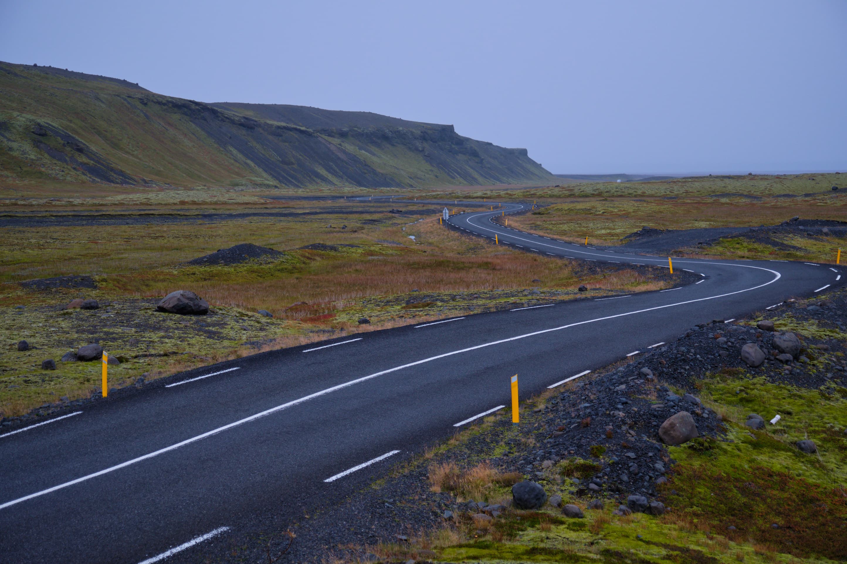 Winding road through dark lava moorland toward mesa cliff