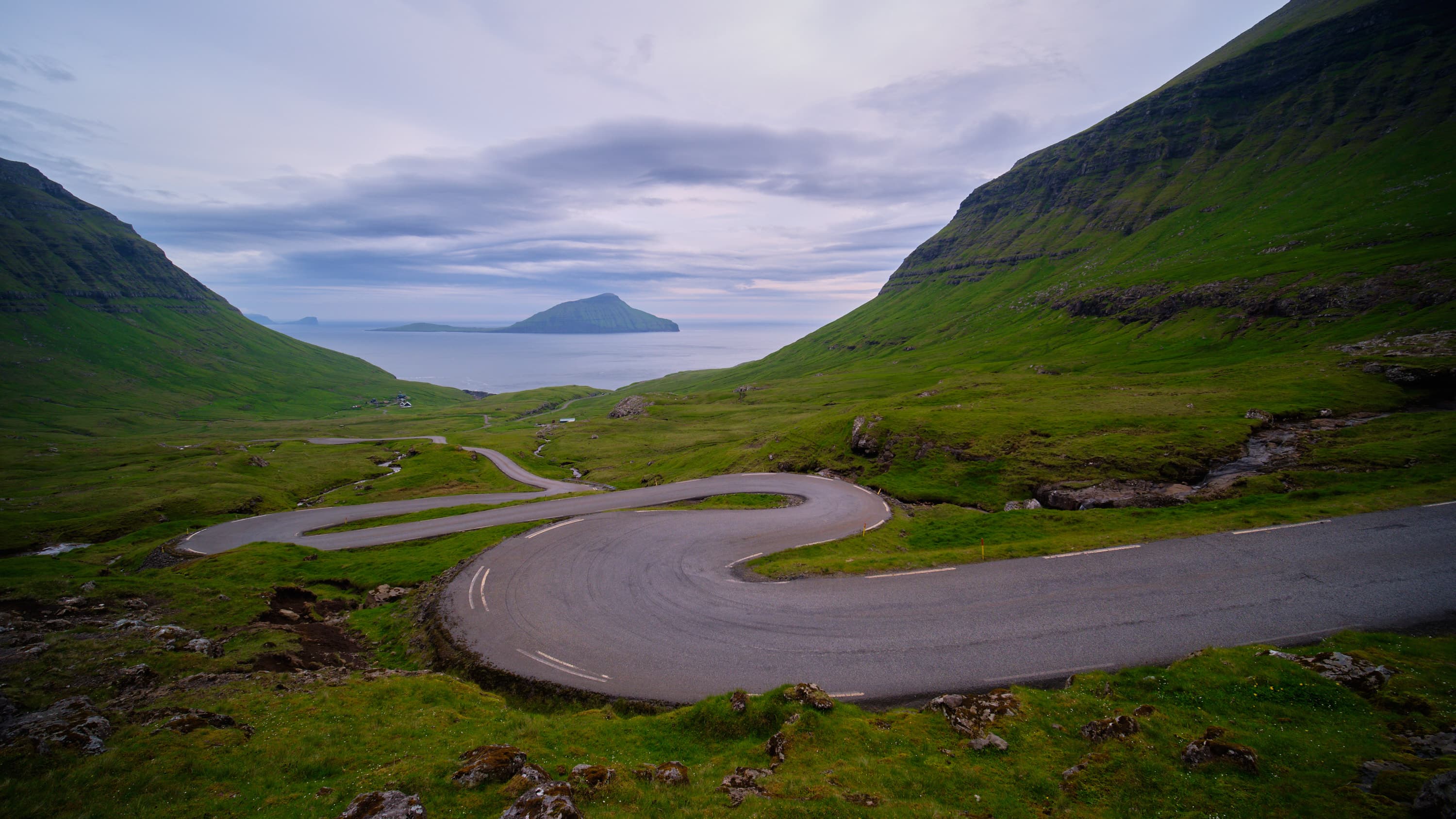 Winding road through green Faroese fjord valley to the sea