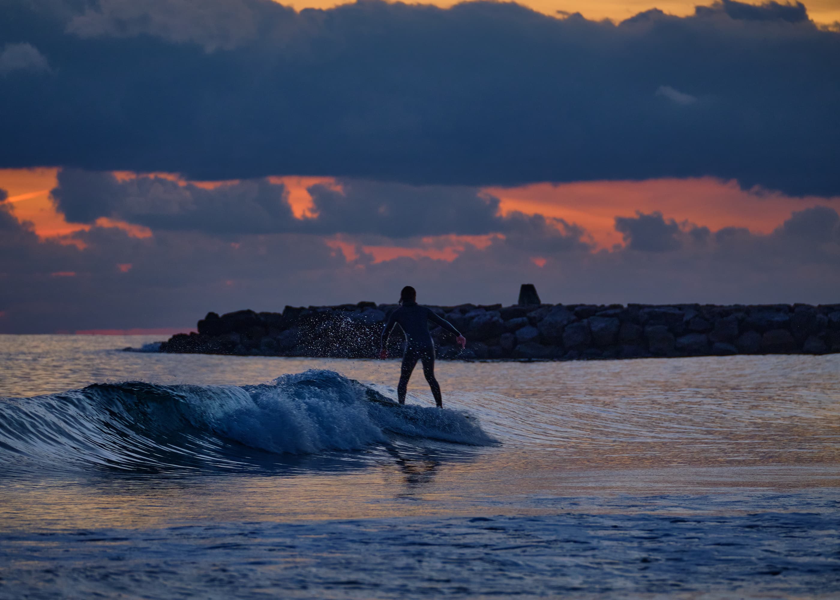 Surfer silhouette on breaking wave at dramatic sunset
