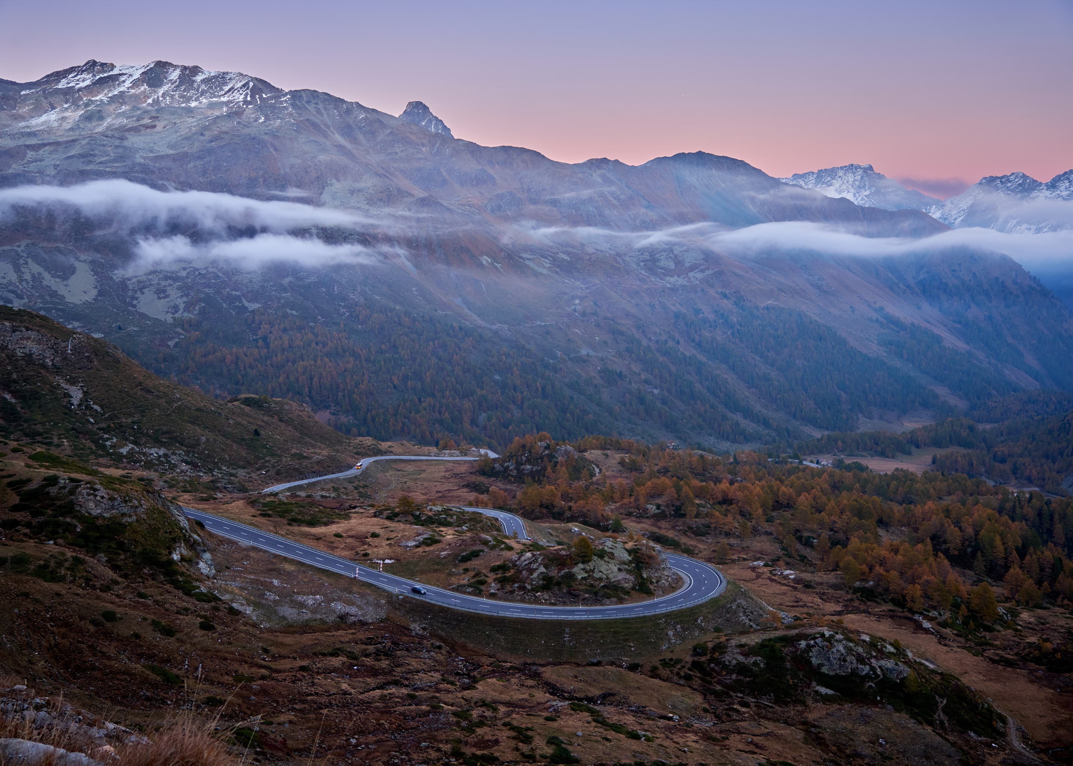 Serpentine alpine pass road at dawn, pink sky, valley mist