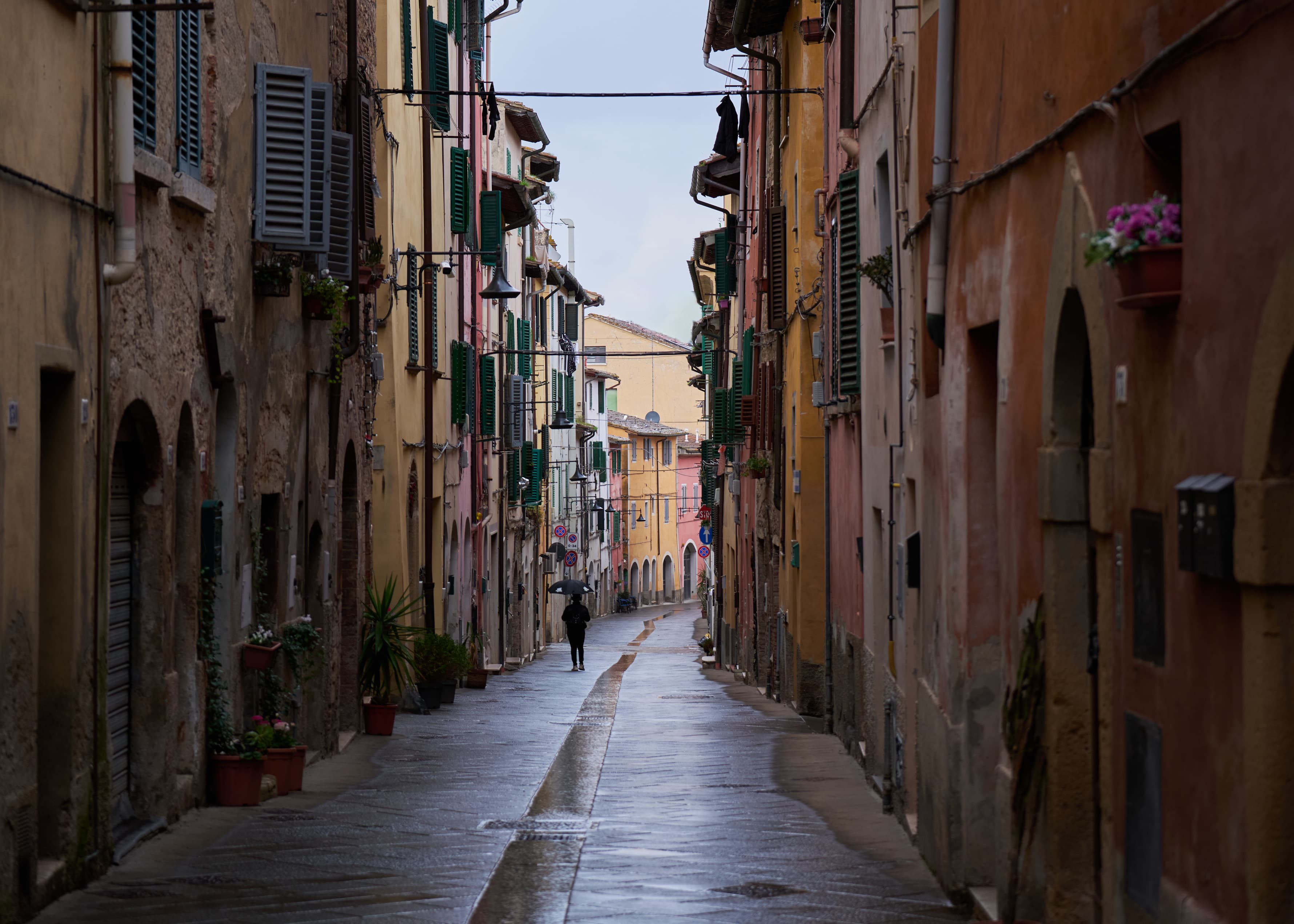 Lone figure with umbrella in rain-soaked Tuscan alley