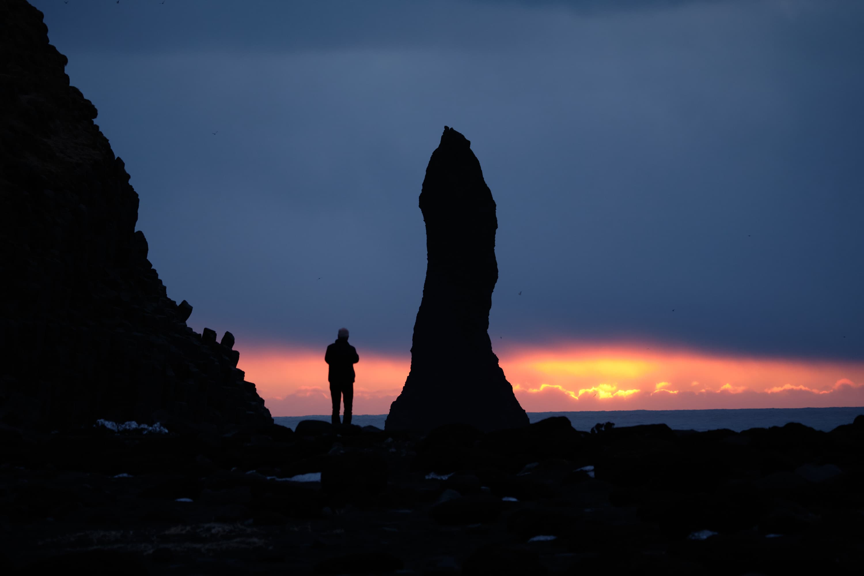 Silhouette figure and sea stack at fiery Atlantic sunset